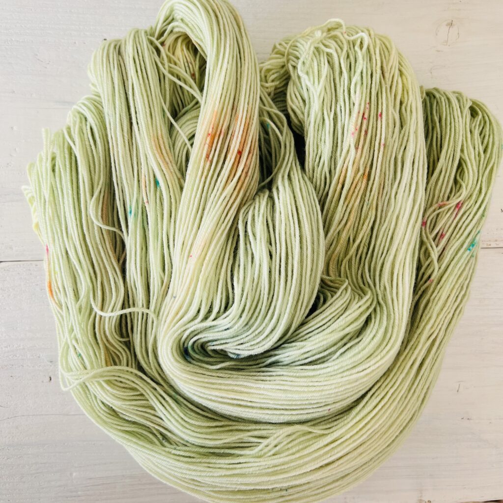 やわらかイエローの光が差し込むパステルくすみグリーンのグラデーションの手染め毛糸のカセをほどいた色の入り方