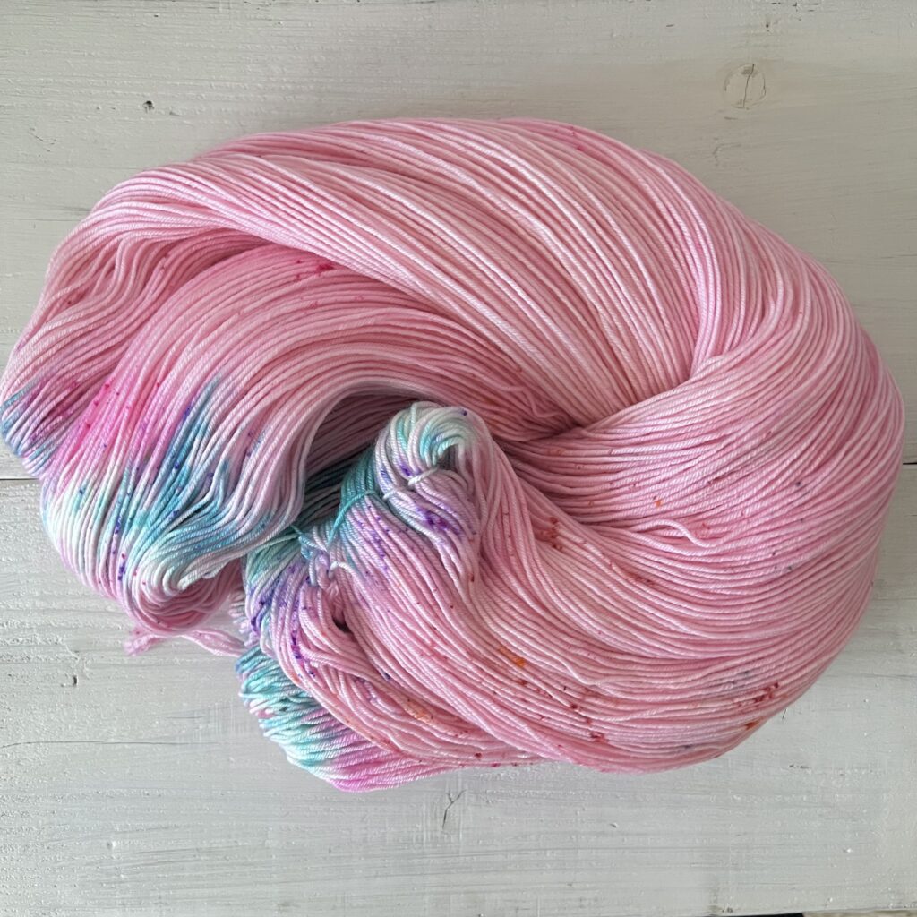 ピンクに抜染の白とティールなどのグラデーションが美しい手染め毛糸のカセをほどいた色の入り方